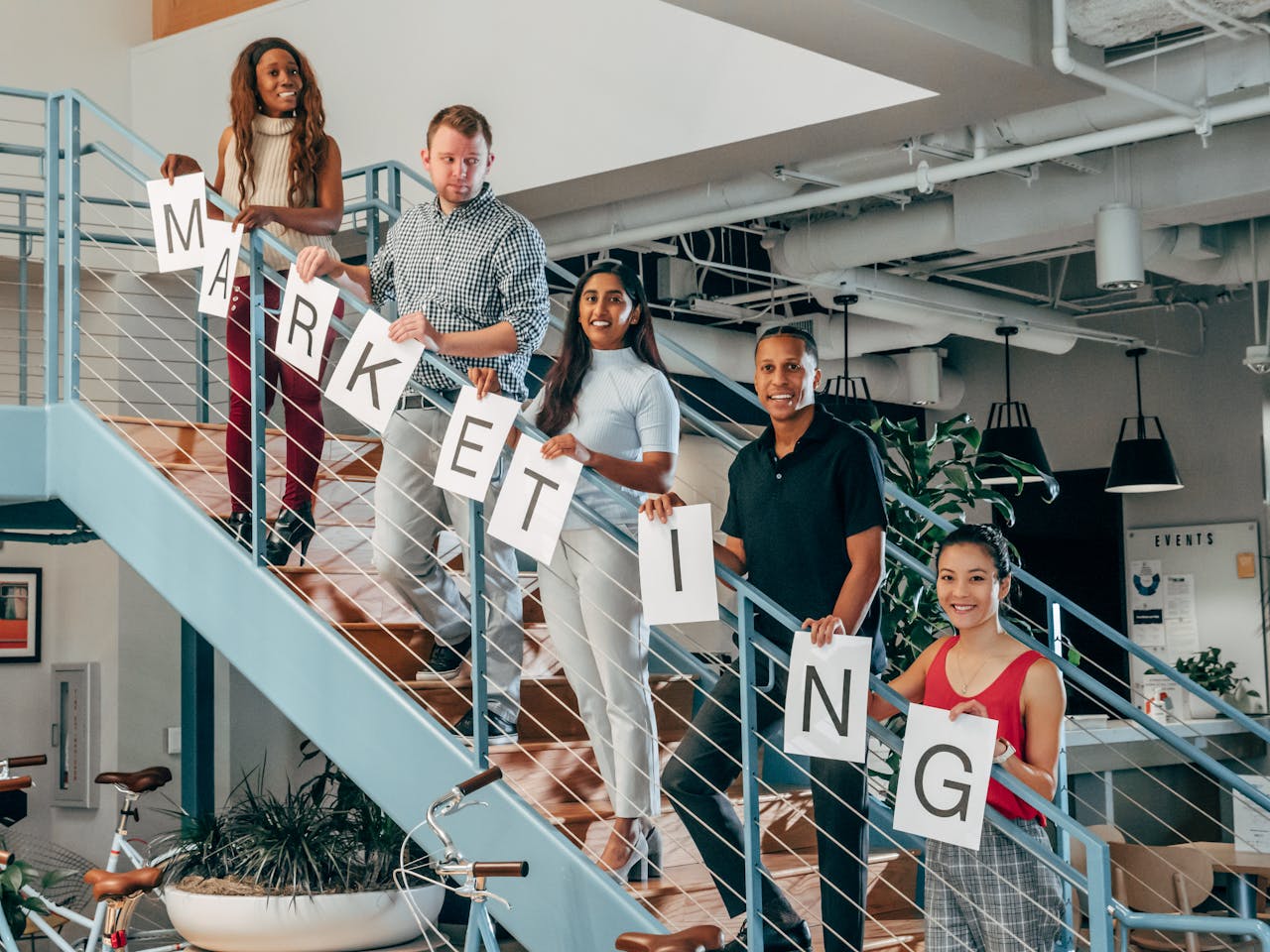 A diverse group of professionals holding marketing signs on an office staircase.